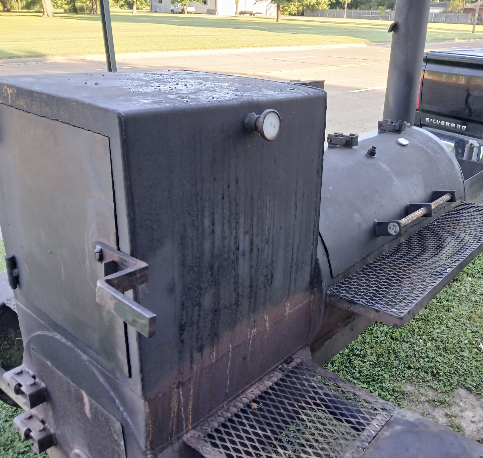 The JK Southern Cooking barbecue smoker outdoors — a black steel firebox and long cooking chamber with tall smokestack and mesh side shelves